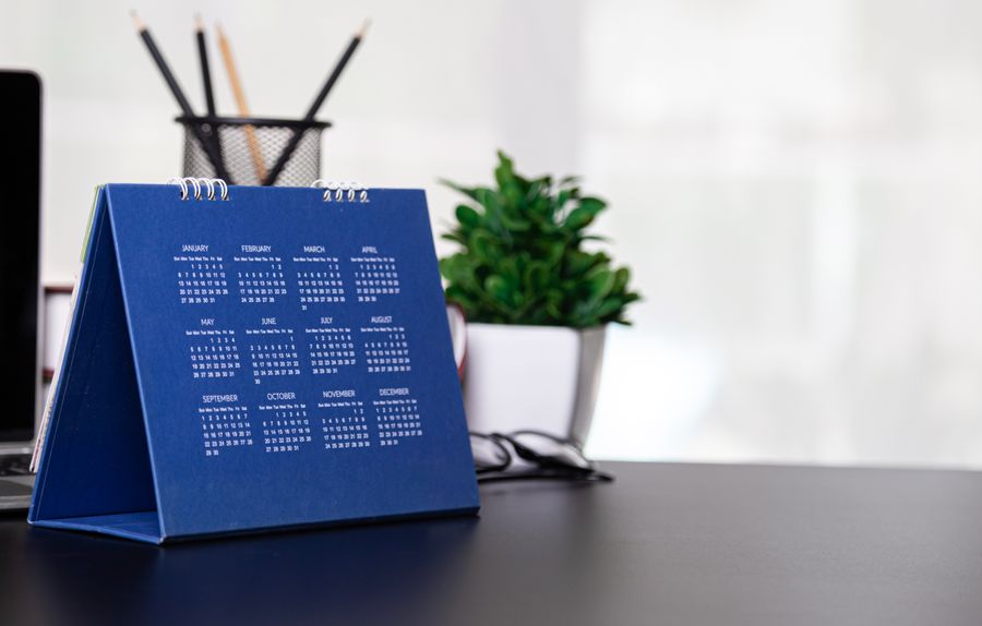 Image of a navy blue calendar on a desk with a green plant behind it 